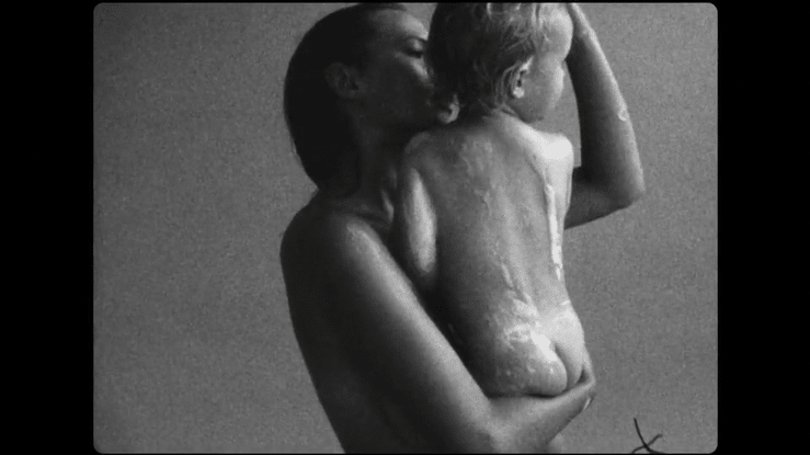 A woman embraces a child in a monochromatic image with visible film grain and scratches, capturing a tender, intimate moment.