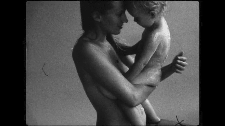 A woman embraces a child in a monochromatic image with visible film grain and scratches, capturing a tender, intimate moment.