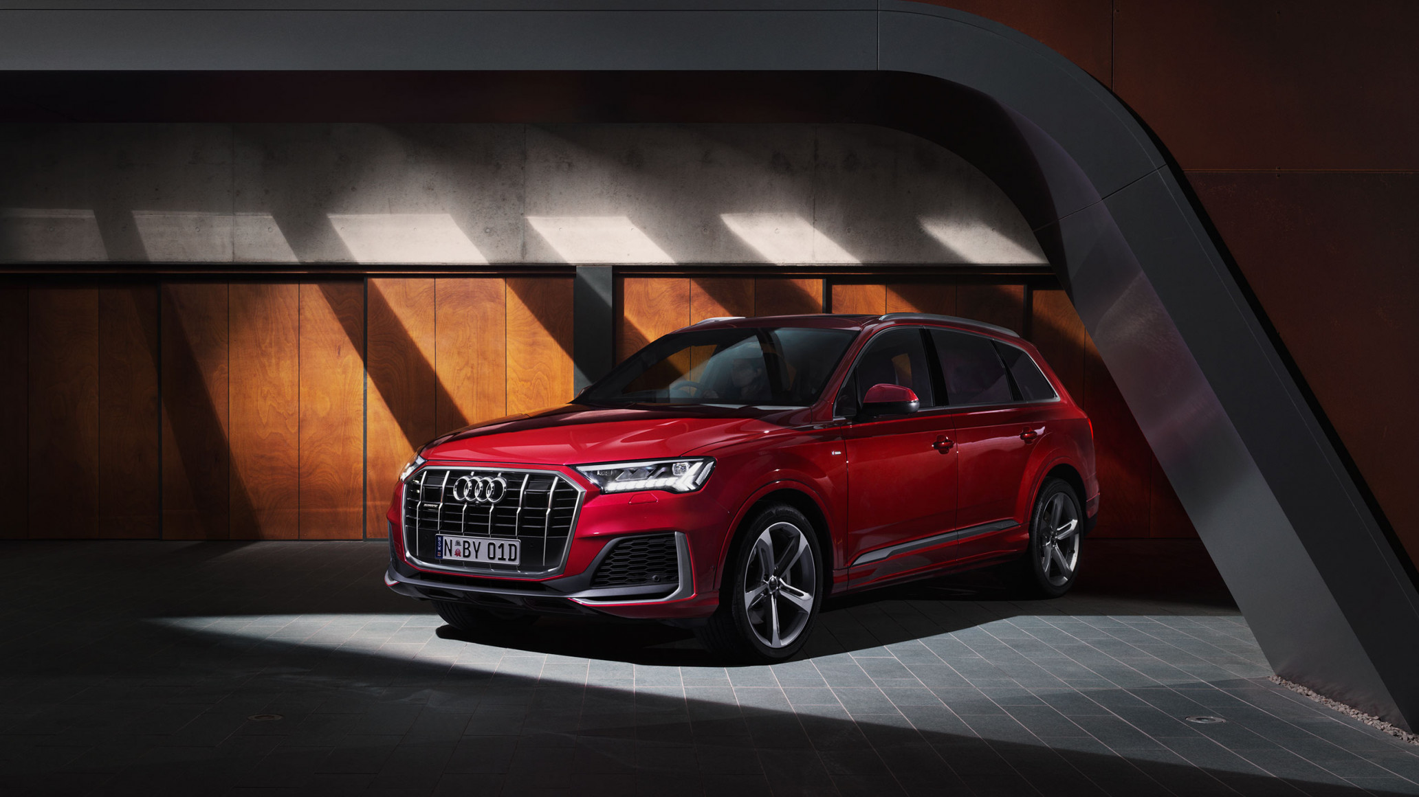 A luxurious red Audi Q7 SUV is parked indoors under modern architecture, illuminated by bright light and reflecting gloss and design.