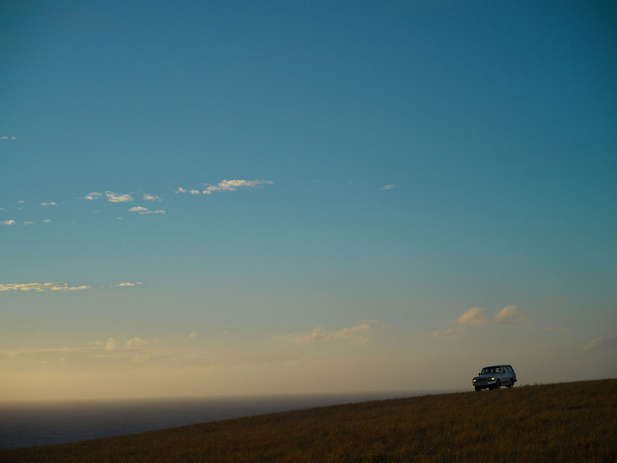 Vehicle on a grassy hill under a blue sky near a body of water. Landscape with a car in a natural setting.
