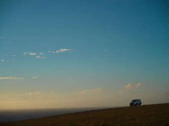 A vintage SUV driving along a grassy ridge under a vast clear blue sky during sunset, photographed by Andreas Smetana.