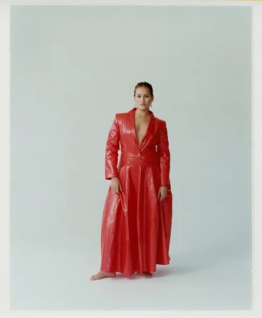 Full-length portrait of a woman standing in a glossy red long coat against a seamless white studio background