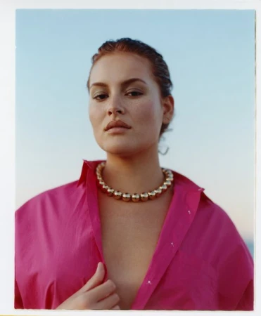Portrait of a woman wearing a pink shirt and a chunky gold bead necklace against an outdoor sky background