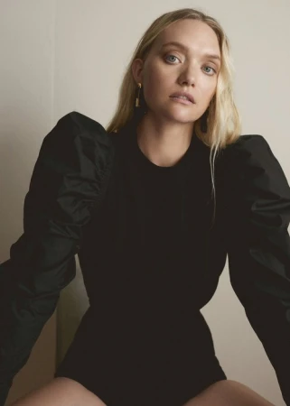 Portrait of a blonde woman wearing a black puff-sleeve top against a neutral wall by photographer Kelly Geddes.