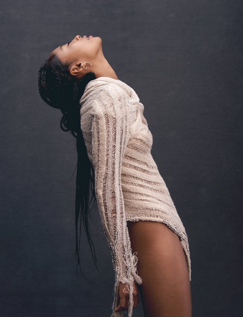 Portrait of a woman with dark hair wearing a textured off-white dress, looking upward in a photo studio with a dark background.