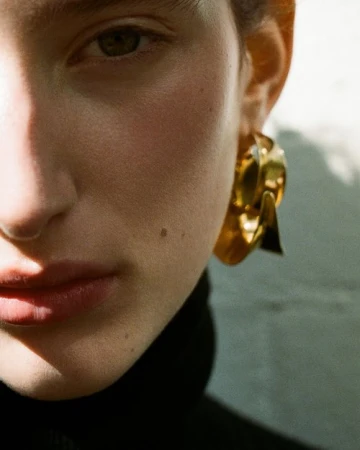 Close-up portrait of a woman wearing large gold hoop earrings and a dark turtleneck photographed by Kelly Geddes.