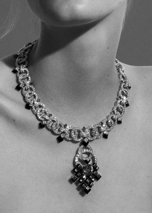 Close-up shot of a woman wearing a diamond necklace with black gemstones, emphasizing the necklace's intricate design and monochrome aesthetic.