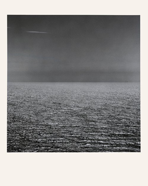 Monochrome photograph of an ocean view under an overcast sky, the horizon line splitting the frame into equal parts of sea and sky.