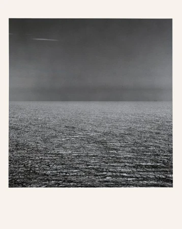 Monochrome photograph of an ocean view under an overcast sky, the horizon line splitting the frame into equal parts of sea and sky.