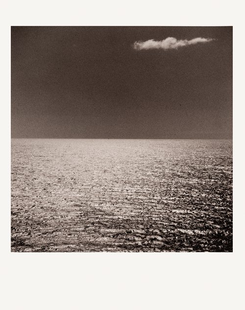 Monochromatic photo of a still ocean under a dark sky with a single cloud, emphasizing stillness, minimalism, and serene natural beauty.