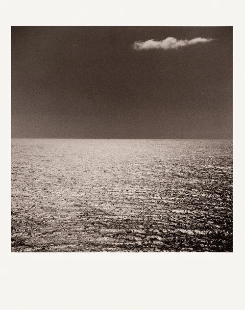 Monochromatic photo of a still ocean under a dark sky with a single cloud, emphasizing stillness, minimalism, and serene natural beauty.