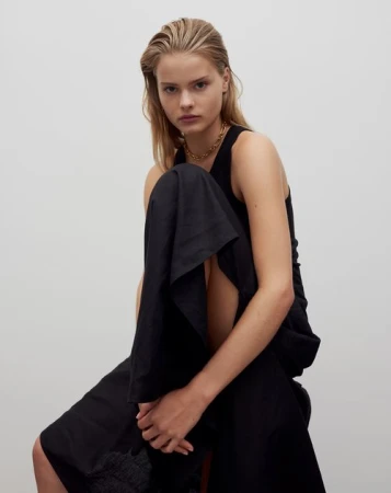 Model with slicked-back blonde hair wearing a black sleeveless top against a plain white background by Kelly Geddes.