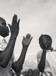 Monochrome low angle photograph of two children in white shirts holding up hands against an overcast sky