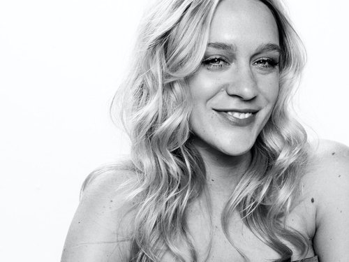Monochrome portrait of a blonde adult woman smiling with bright studio lighting and a shallow depth of field for fashion and beauty content.