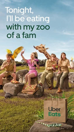 Whimsical ad with four people and various animals around food and an Uber Eats bag in a grassy field on a sunny day.