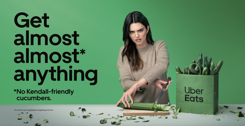 Uber Eats advertisement features Kendall Jenner awkwardly chopping a cucumber with many cucumbers in a bag and food delivery service logo.