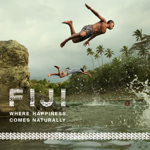 Two athletic men jump into tropical ocean waters off a rocky cliff. Palm trees and island vegetation form the scenic backdrop.