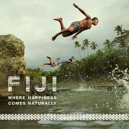 Two athletic men jump into tropical ocean waters off a rocky cliff. Palm trees and island vegetation form the scenic backdrop.