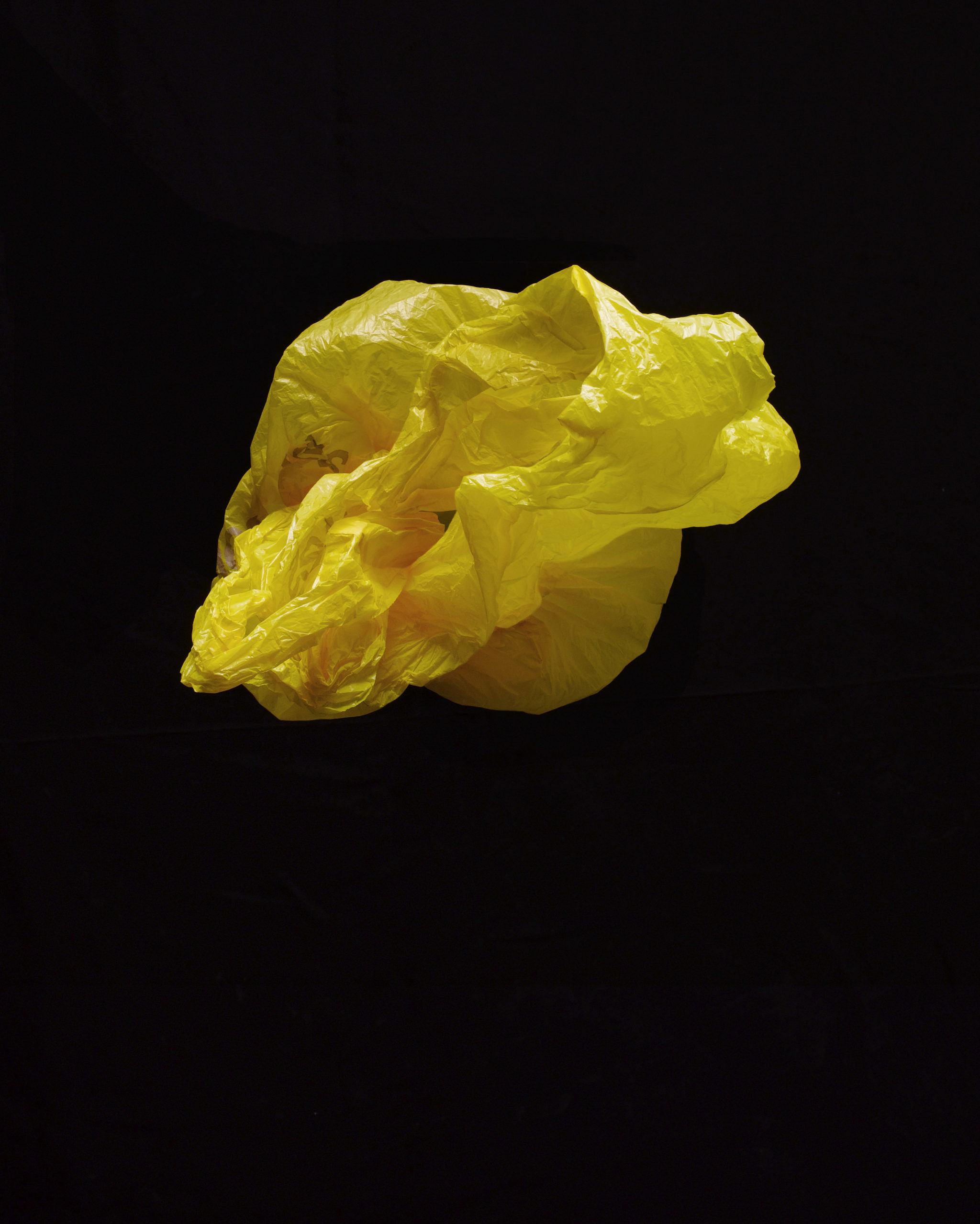 Close-up of a crumpled yellow plastic bag floating in the air against a solid black background, creating a stark contrast.