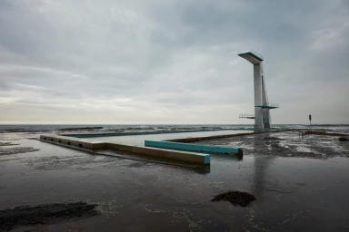 Concrete ocean pool with a tall diving tower under an overcast sky by Danny Eastwood in Sydney.
