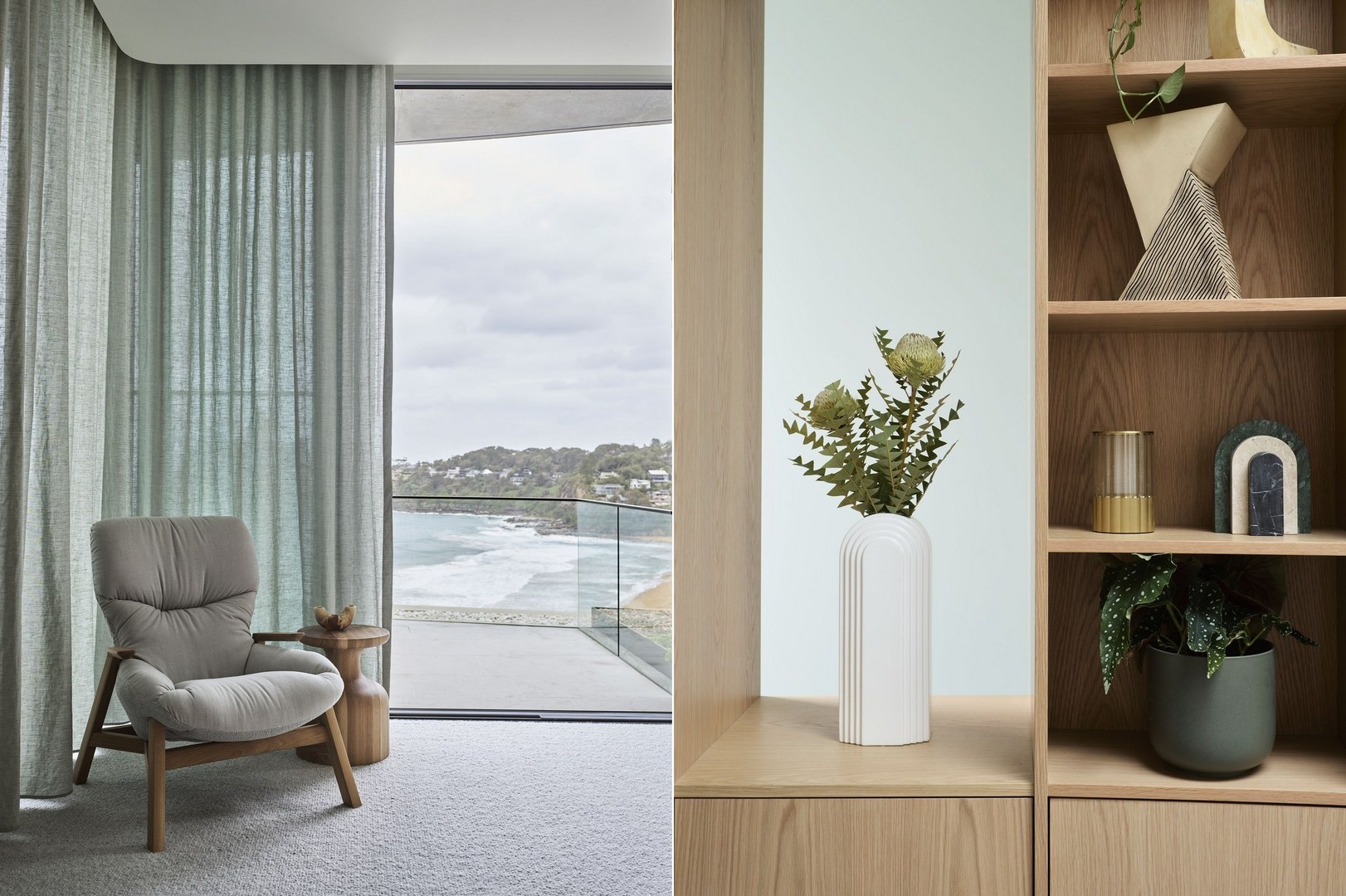 Living room interior with a grey armchair, wood side table, shelving unit with decorative objects, and ocean view through large windows.