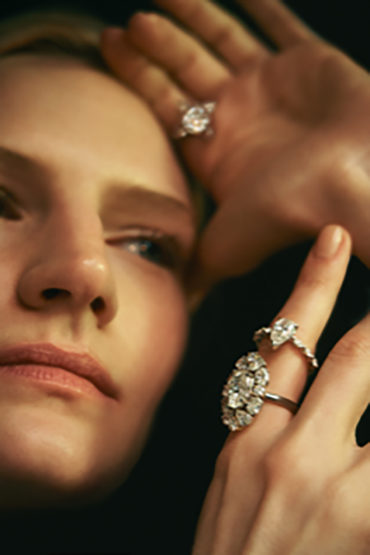 Close-up portrait of a blonde adult woman with diamond rings on her fingers, black background, soft studio lighting, beauty shot.