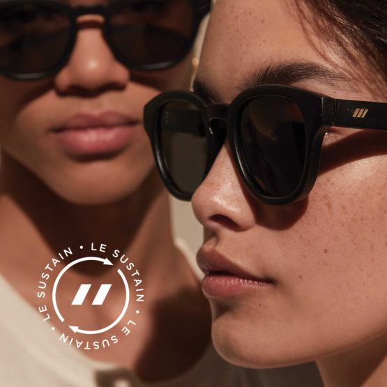 Two adults wearing dark sunglasses in a close-up shot. One person is slightly out of focus in the background.