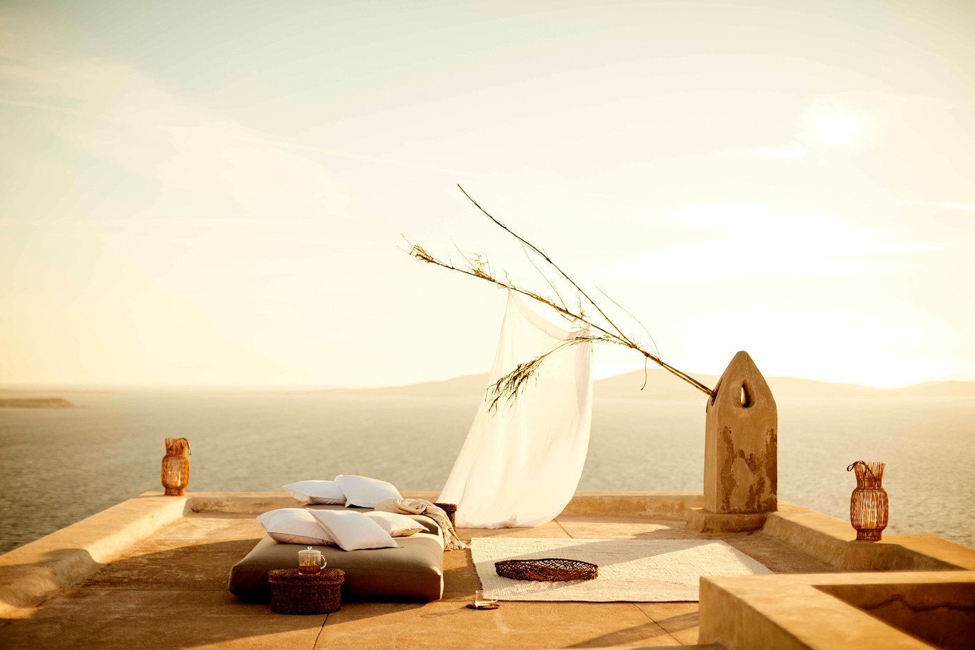 Outdoor daybed setup on a rooftop terrace with pillows, a white curtain, and sea views creating a tranquil and inviting space.