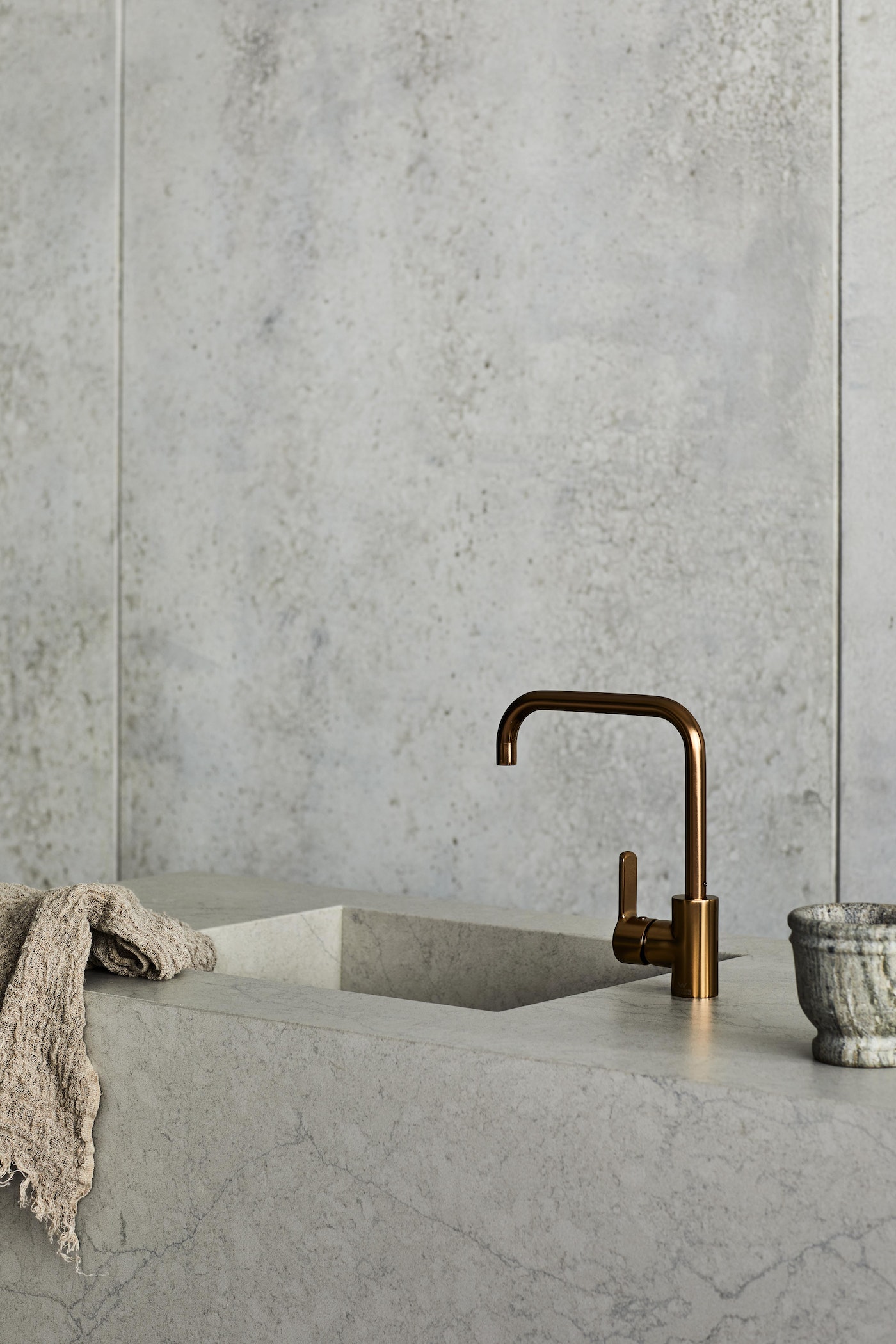 Minimalist kitchen interior featuring a copper faucet, marble countertop, neutral-toned dishcloth, and textured gray marble walls.