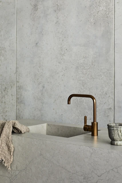 Minimalist kitchen interior featuring a copper faucet, marble countertop, neutral-toned dishcloth, and textured gray marble walls.