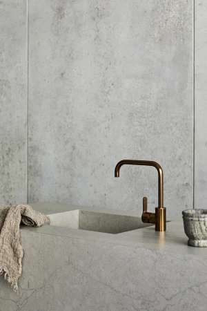 Minimalist kitchen interior featuring a copper faucet, marble countertop, neutral-toned dishcloth, and textured gray marble walls.