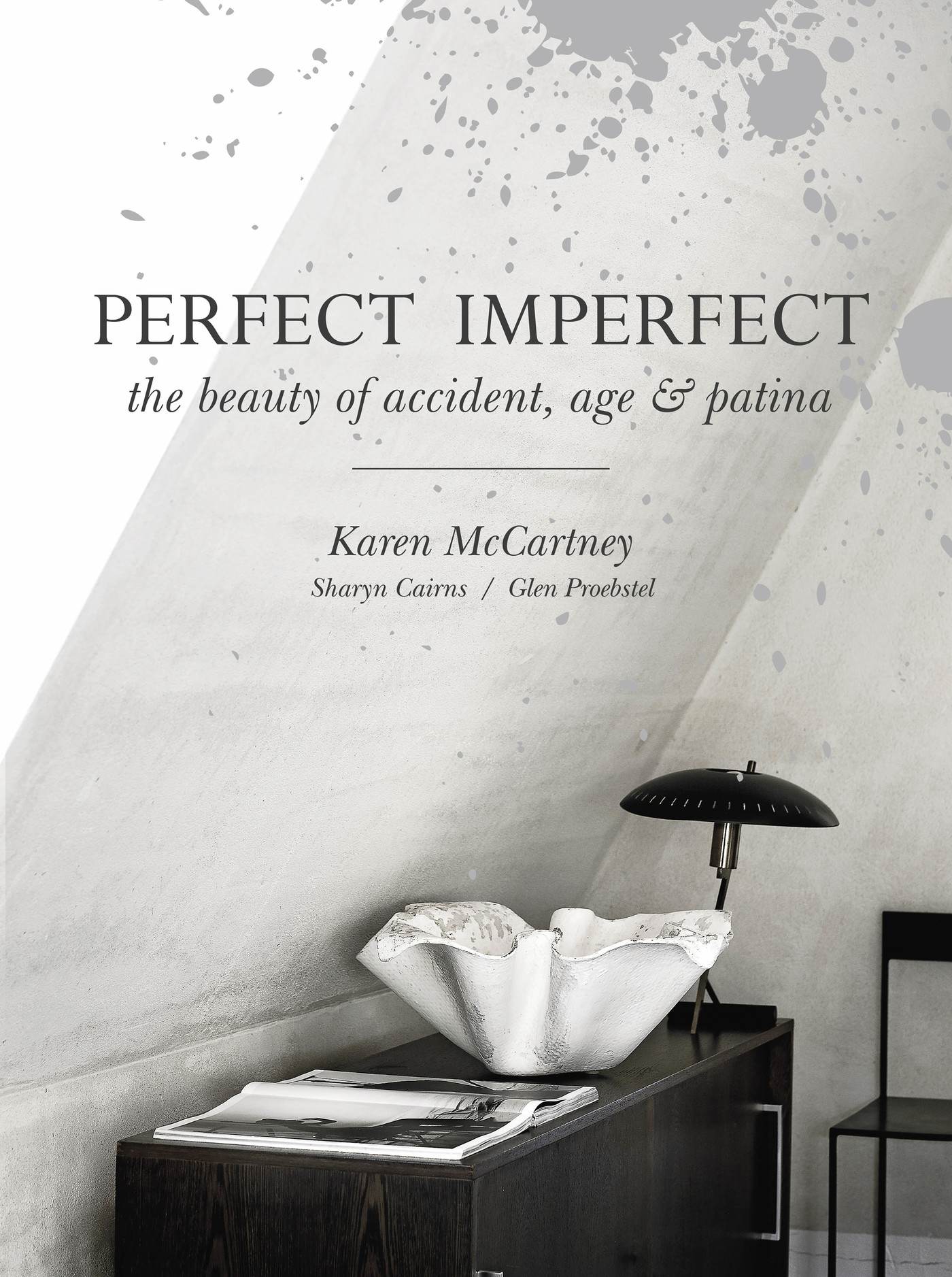 Book cover featuring a white bowl and a black lamp atop a dark wood cabinet against a textured gray wall, minimalist interior design.