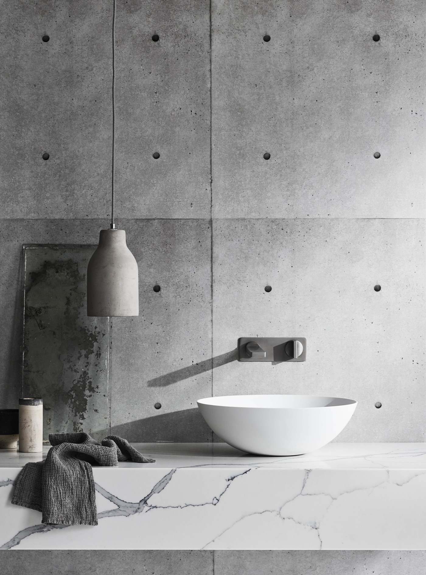 Bathroom interior featuring a white vessel sink, concrete accent wall, gray pendant light, and marble countertop for an elegant look.