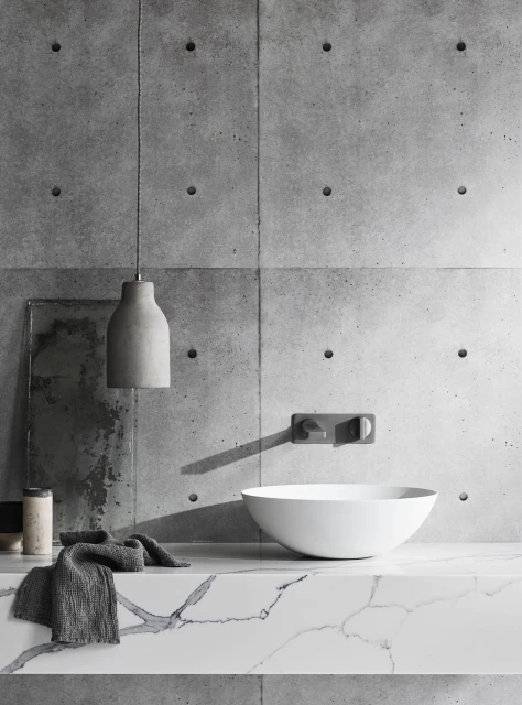 Bathroom interior featuring a white vessel sink, concrete accent wall, gray pendant light, and marble countertop for an elegant look.