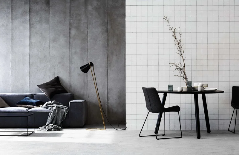 Interior styling by Glen Proebstel showing a dark grey sofa against a concrete wall and a dining table against white tiles