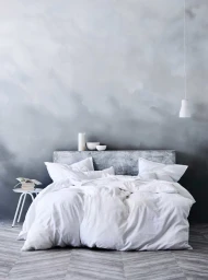 White made bed against a grey watercolor wall with small white bedside table and hanging pendant lamp