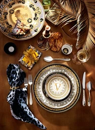 Overhead flat lay of an opulent tablescape with gold and white porcelain plates, cutlery, candles, and gilded palm fronds styled by Glen Proebstel.
