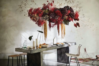 Large suspended floral installation in deep reds above a long stone dining table styled with vases and fruit by Glen Proebstel.