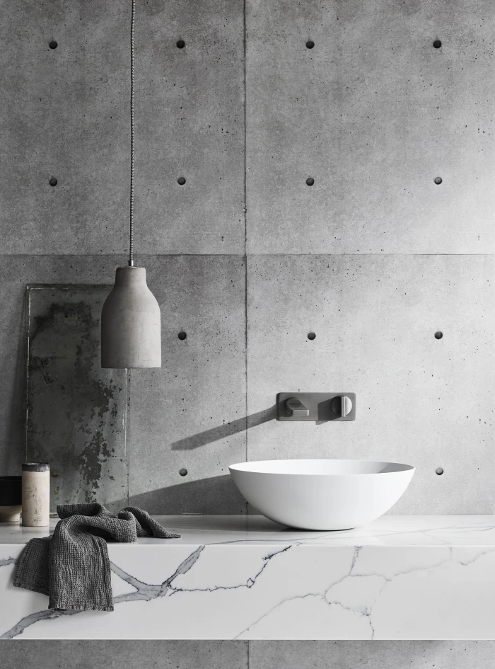 Minimalist bathroom interior featuring a white vessel sink on a marble countertop against a raw concrete wall.