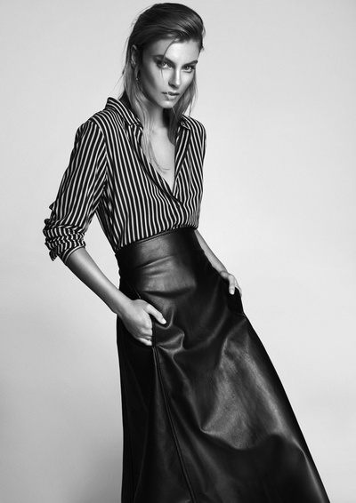 Black and white studio shot of a woman in a striped shirt and leather skirt. Hands in pockets, looking at the camera, fashion pose.
