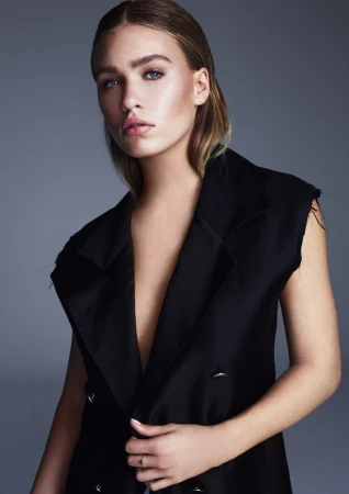 Woman in sleeveless black top with slicked-back blonde hair against a grey background, make-up by Isobel Claire