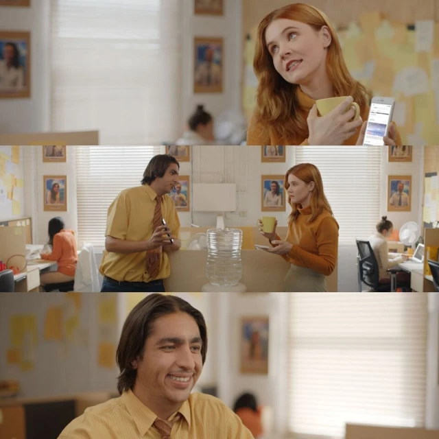 Office scene featuring a red-haired woman holding a coffee cup and smartphone, with a man and other coworkers visible in the background.