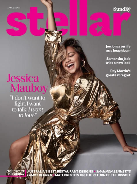 Jessica Mauboy on the cover of Stellar magazine. The adult woman is smiling and wearing a gold trench coat in the indoor shot.