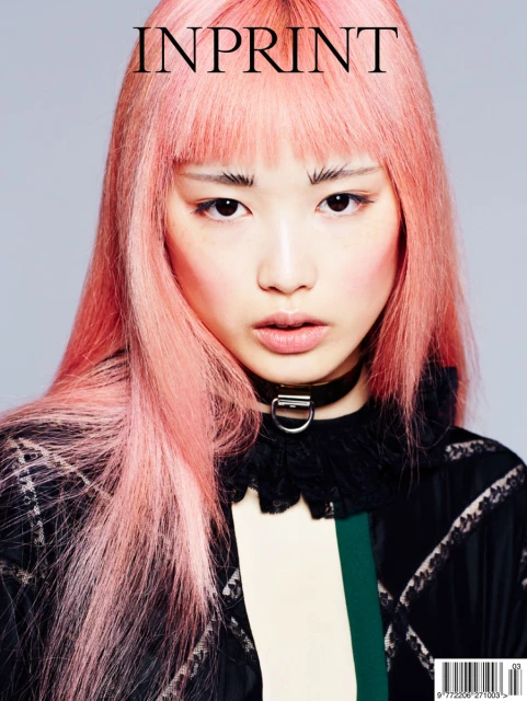 Magazine cover featuring a young Asian woman with pink hair, wearing a black choker and a patterned jacket, against a gray backdrop.