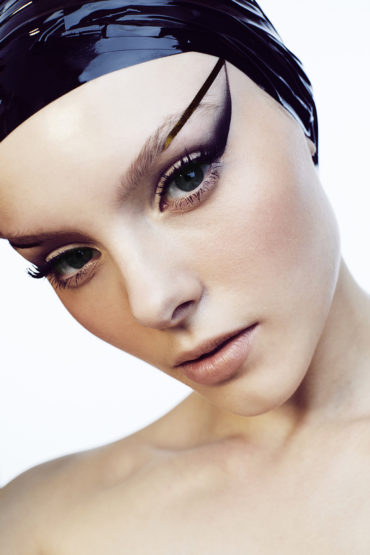 Close-up portrait of a woman with bold purple eye makeup and a glossy purple head covering on a white background, beauty and fashion.