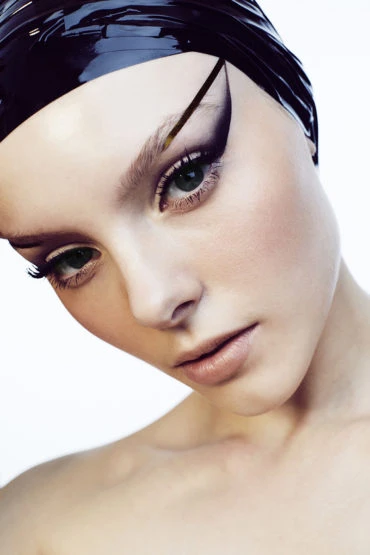 Close-up portrait of a woman with bold purple eye makeup and a glossy purple head covering on a white background, beauty and fashion.