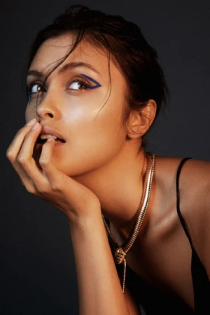 Close-up portrait of a woman with graphic blue eyeliner and a gold snake necklace against a dark background by make-up artist Rae Morris.