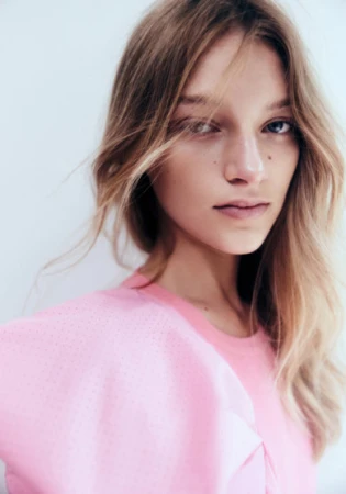 Close up portrait of a young female model with blonde hair wearing a pink top against a white background