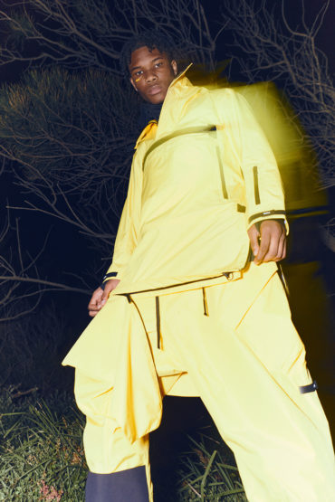 Adult male poses in bright yellow athletic-wear in an outdoor nature setting with dark, moody lighting and blurred motion effects.