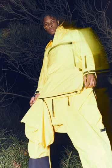 Adult male poses in bright yellow athletic-wear in an outdoor nature setting with dark, moody lighting and blurred motion effects.